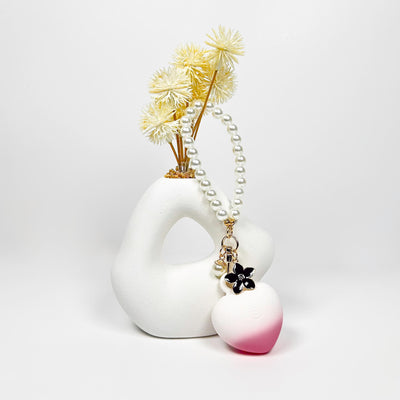 White ceramic vase with dried flowers and a HeartBeat Discreet Mini Vibrator on a light gray background