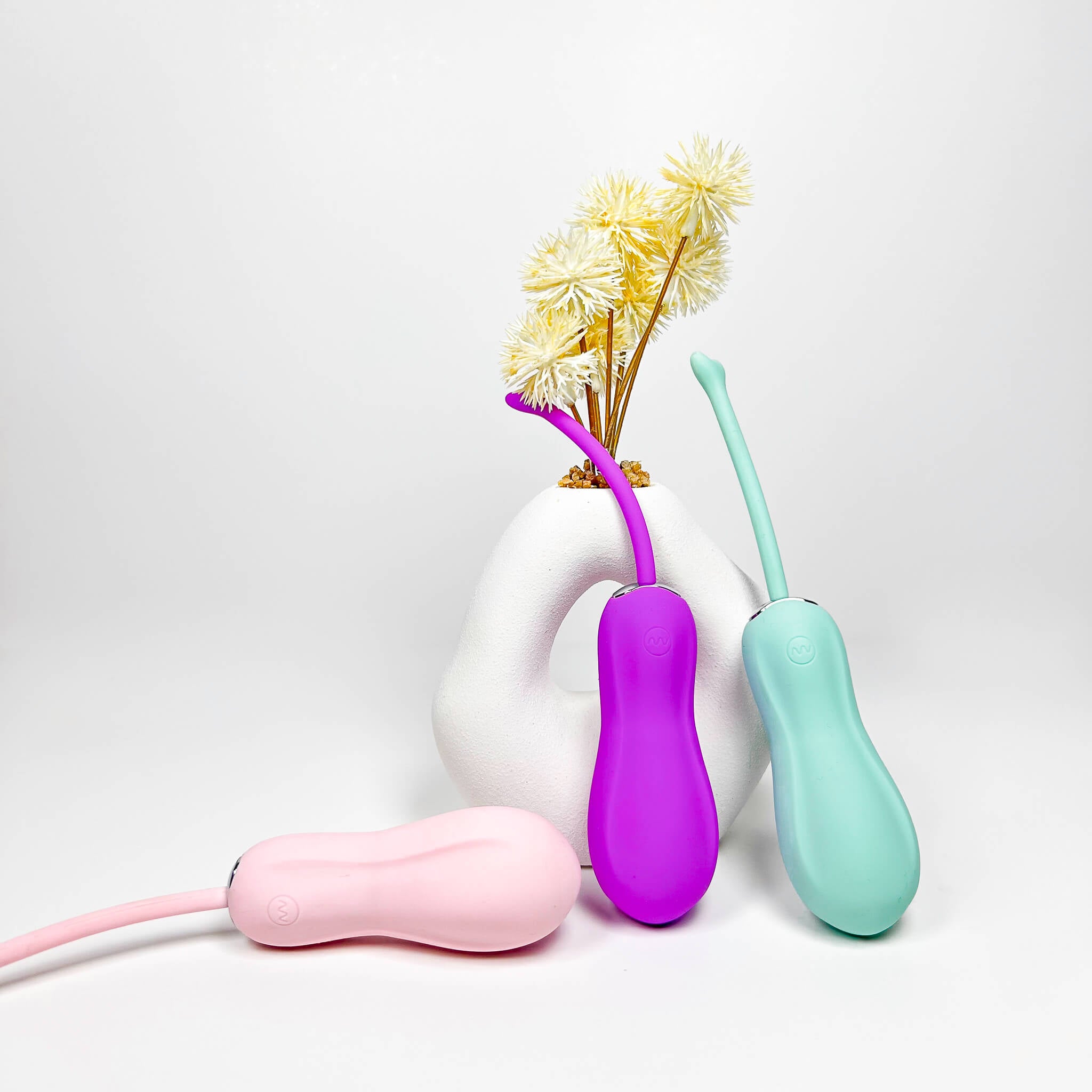 Three colorful Insertable Remote Vibrators on a white background with a vase of yellow flowers.