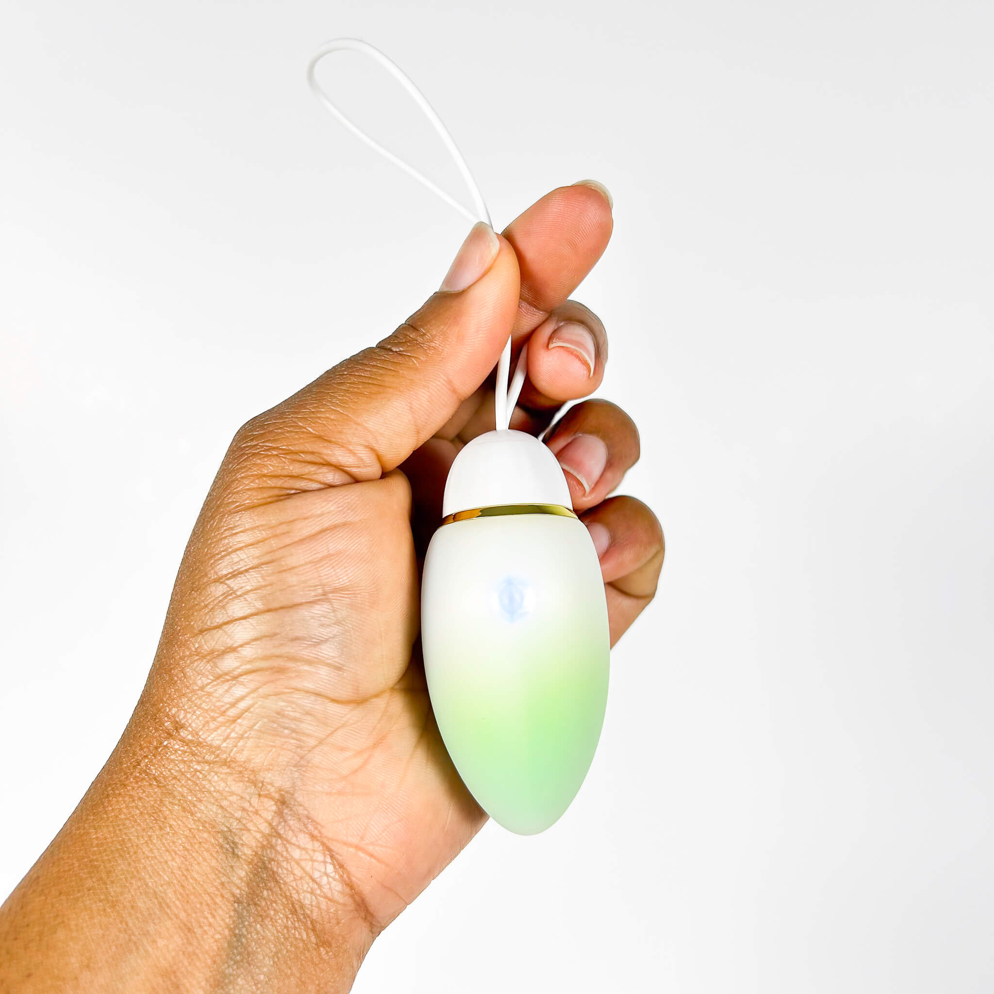 Hand holding a small, oval-shaped JumpStart App-Controlled Jumping Egg Vibrator with a white top and greenish-brown body against a white background