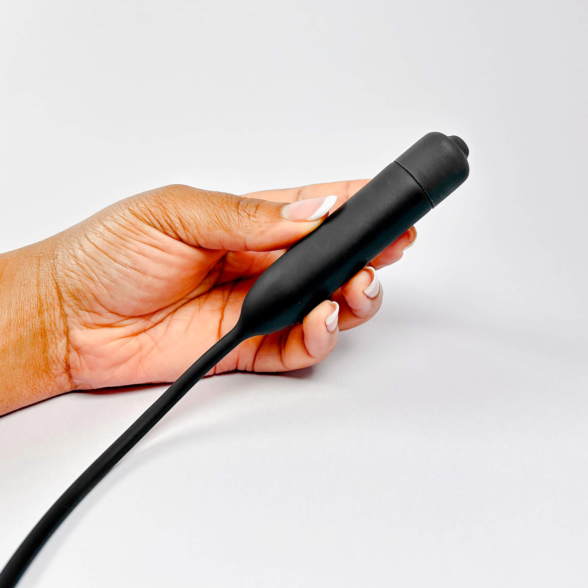 Hand holding a Long Silicone Urethral Vibrator Plug on a light gray background