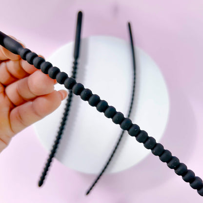 Medium Ribbed Silicone Urethral Plug held by a hand against a pink background