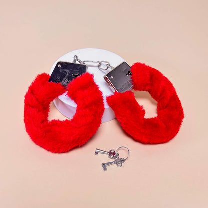 Red fluffy handcuffs with keys on a beige background