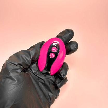Pink remote vibrator held in a black gloved hand against a pink background