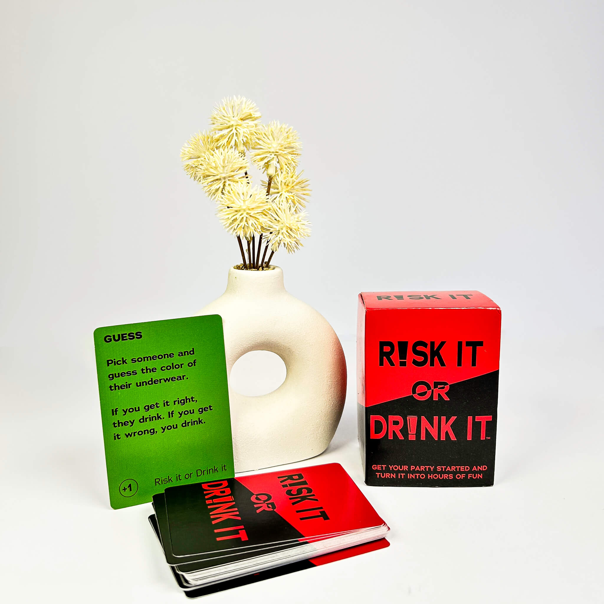 Vase with flowers, 'Guess' card, and 'Risk It or Drink It' game boxes on a white background