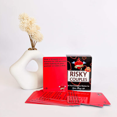 Risky Couples game cards and packaging on a white surface with a decorative vase in the background.