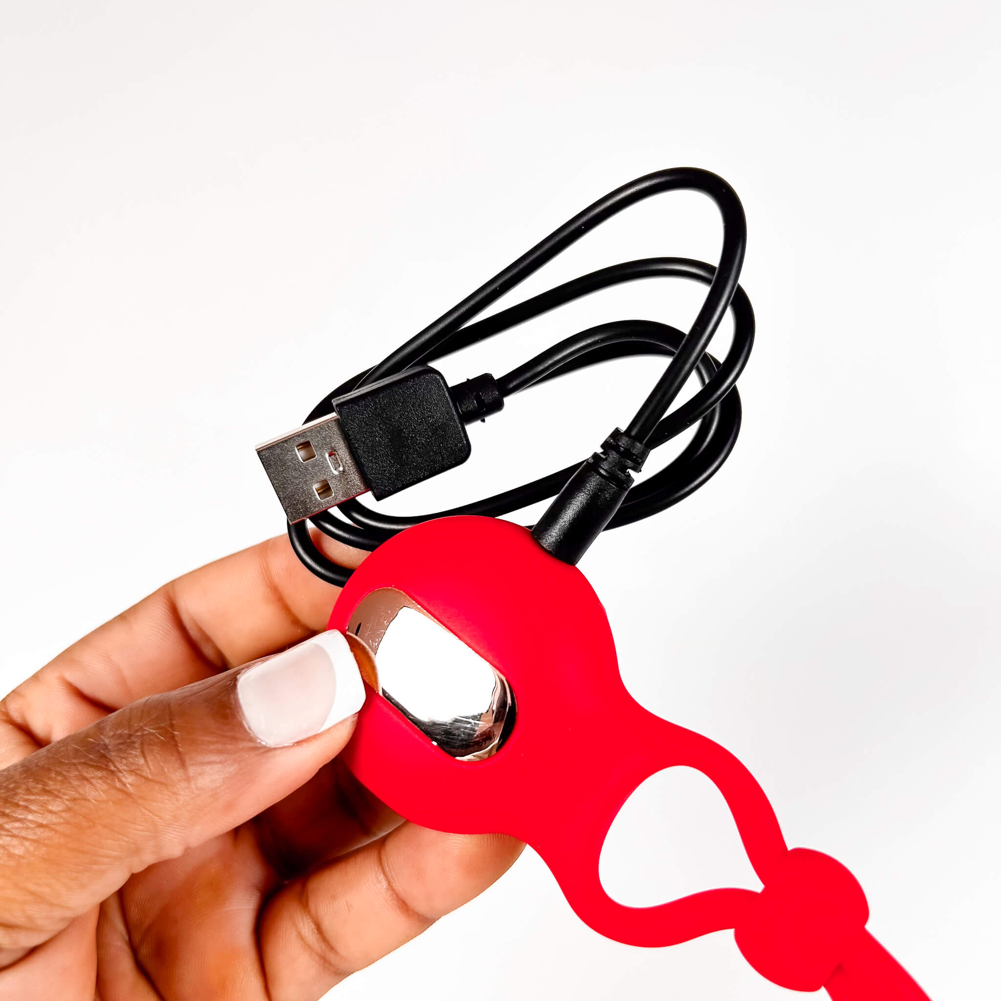 Hand holding a red bottle cock ring with a USB cable attached on a white background