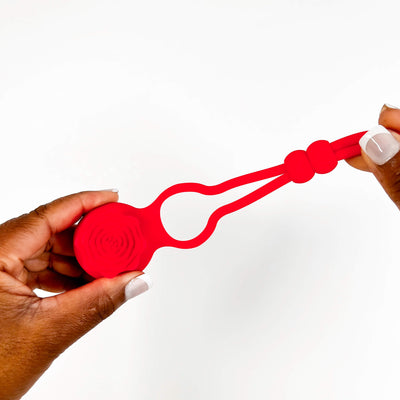Red silicone adjustable vibrating cock rings held by two hands on a white background