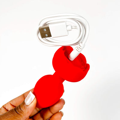 Red vibrating silicone butt plug with a white USB cable on a white background