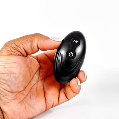 Hand holding a black remote control device on a white background