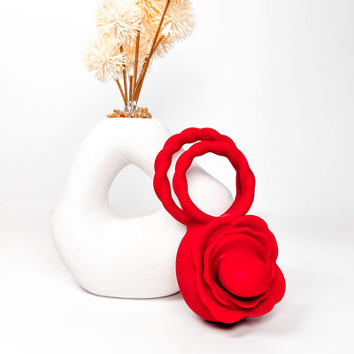 Red RoseLick Rotating Tongue Couples Ring next to a white vase with decorative elements on a light background