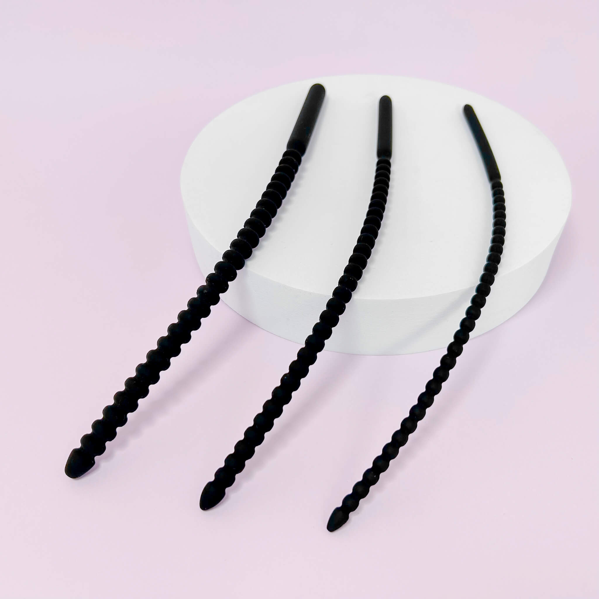 Set of ribbed Silicone Urethral Plugs on a white heart-shaped object against a pink background