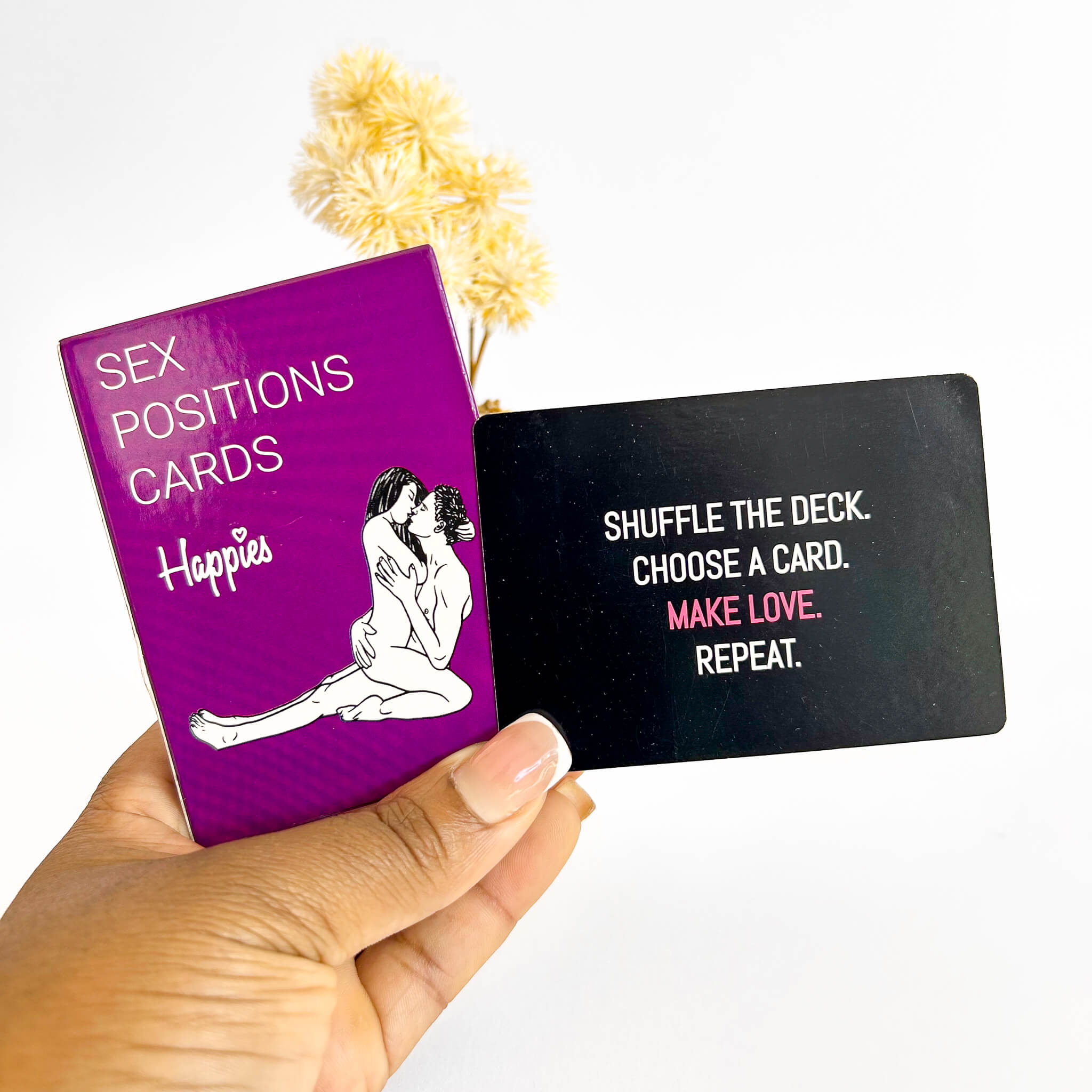 Purple card with 'Sex Positions Cards Happies' text and a black card with humorous text, held by a hand.
