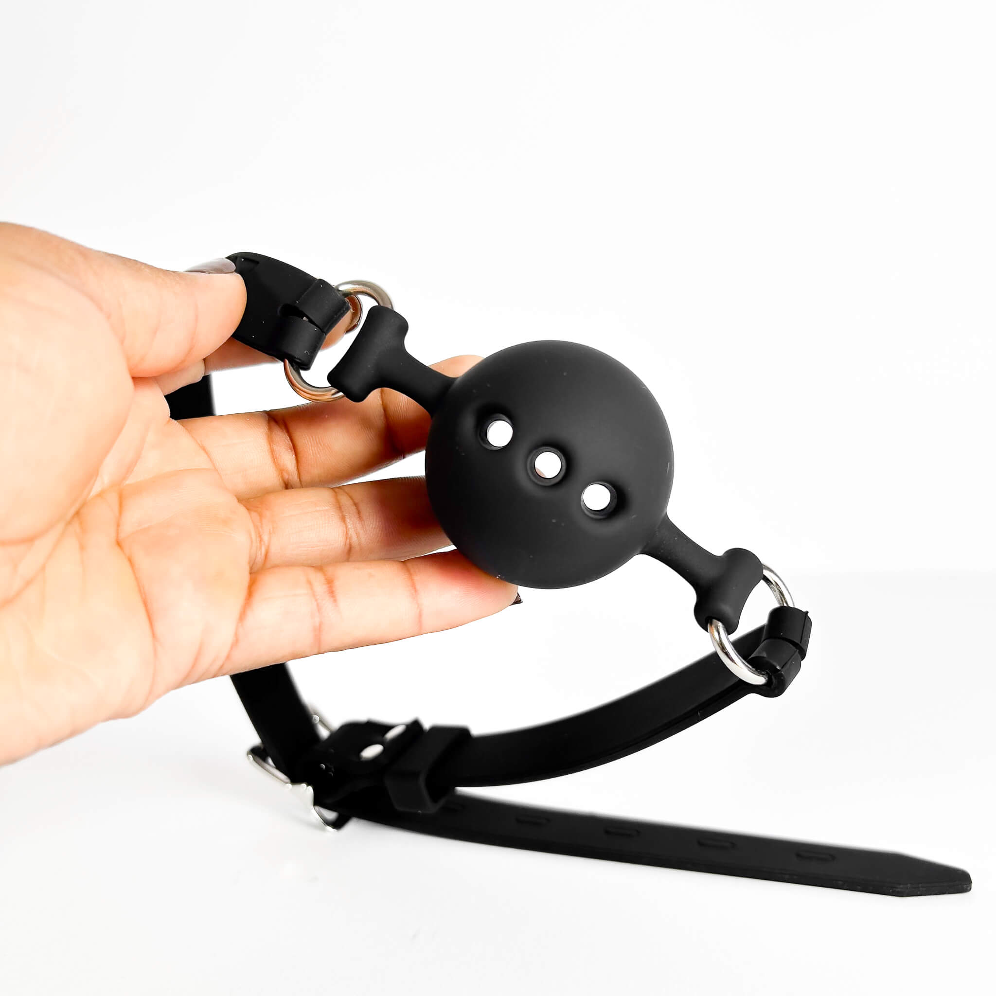 Black silicone ball gag held by a hand on a white background