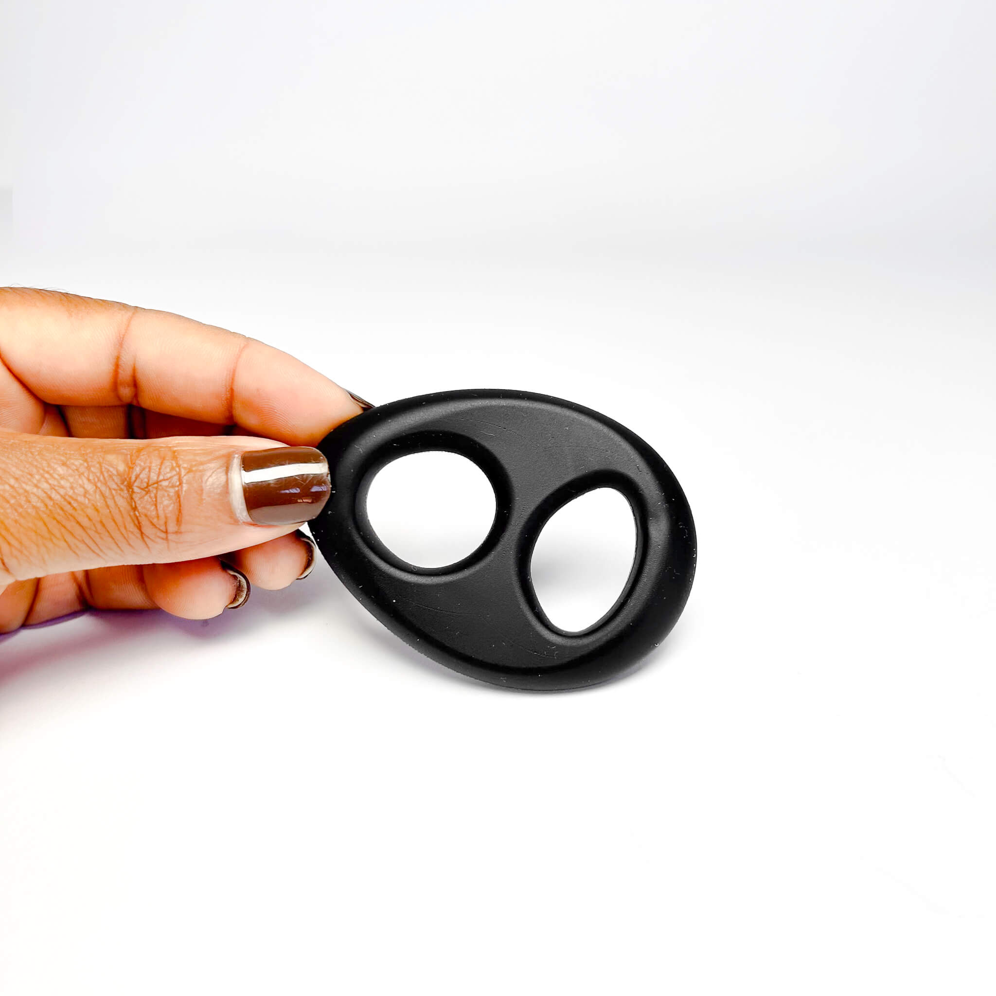 Hand holding a black Silicone dual Cock Ring on a white background