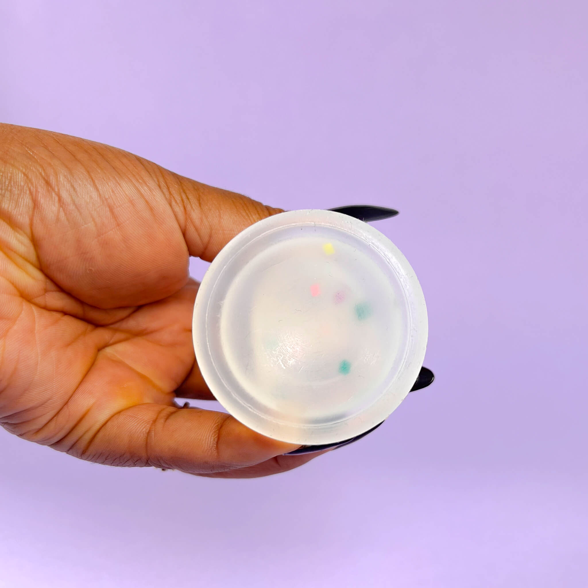 Hand holding a small confetti dildo with colorful dots against a purple background