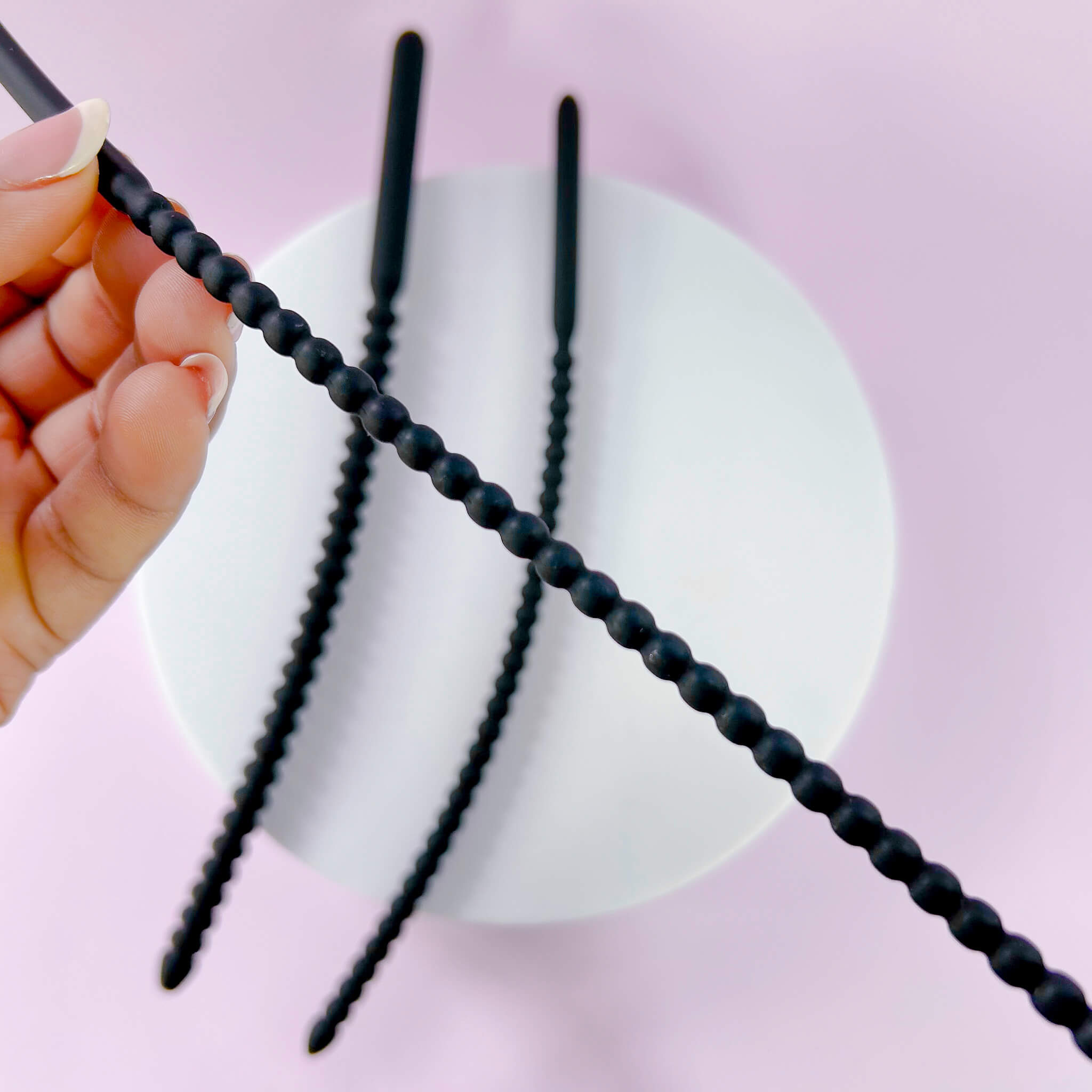 Small Ribbed Silicone Urethral Plug being held against a pink background