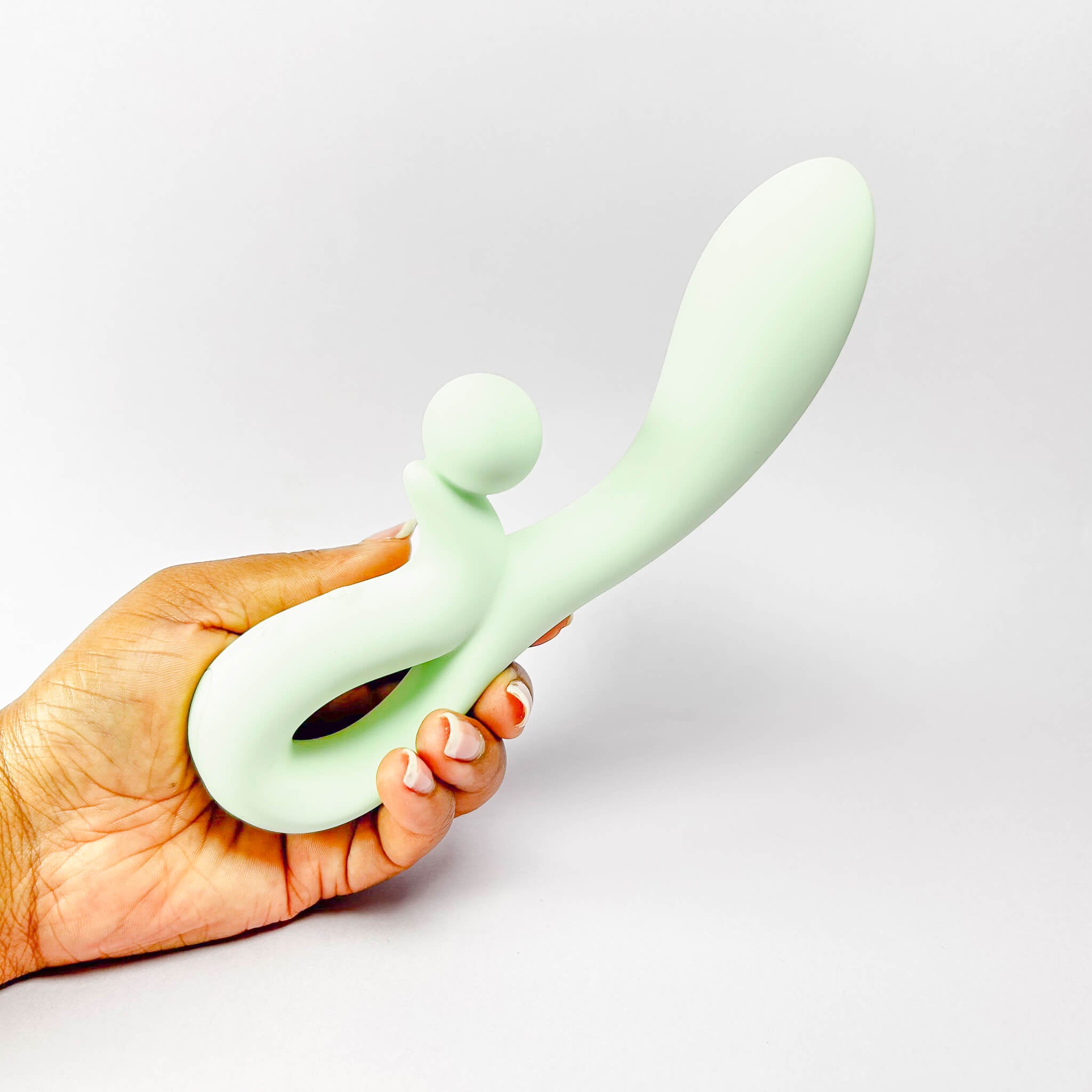 Hand holding a light green silicone rabbit vibrator against a plain background