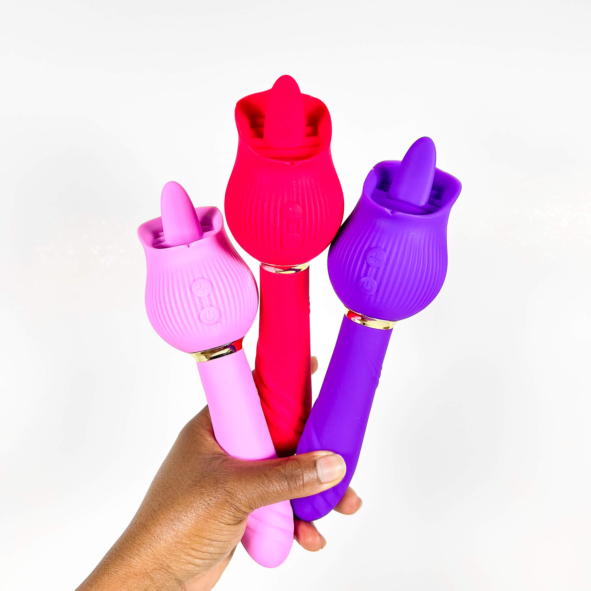 Three colorful silicone TeasePetal 2 in 1 Clitoral Tongue Vibrators held by a hand on a white background