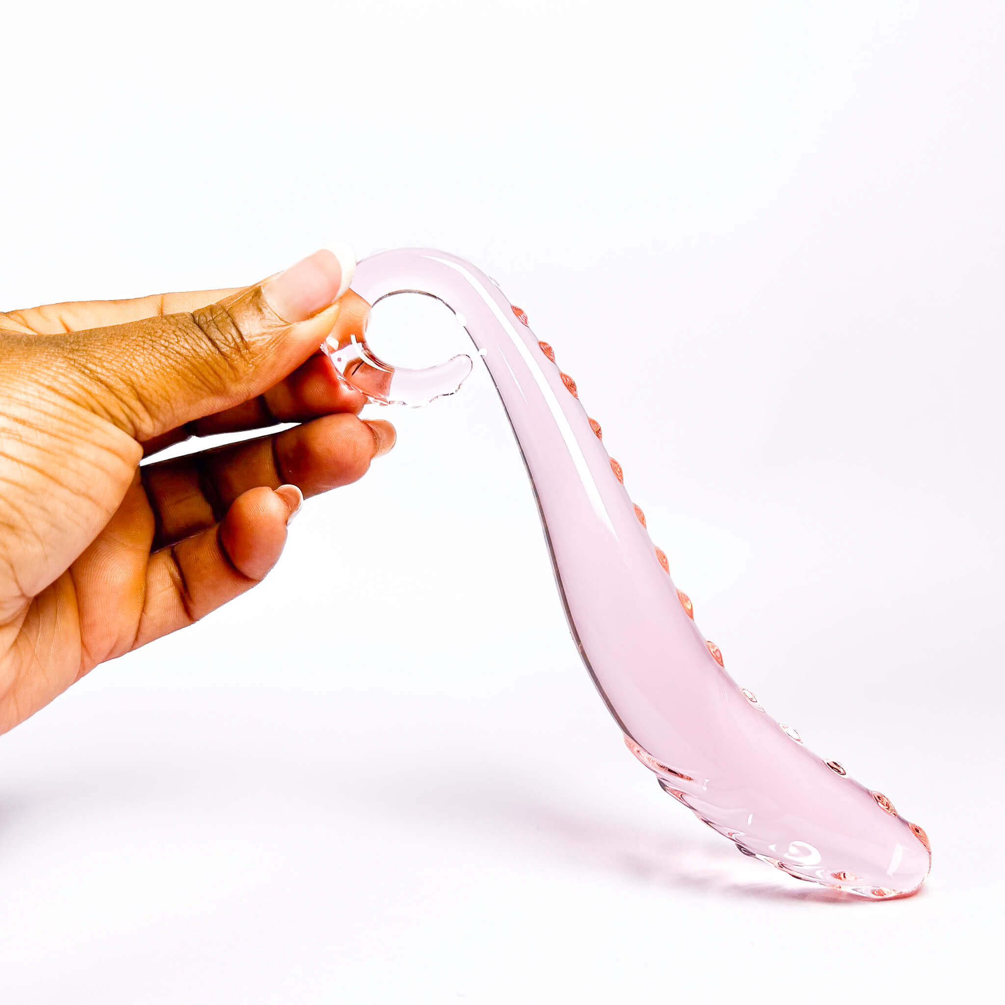 Hand holding a pink glass dildo against a white background