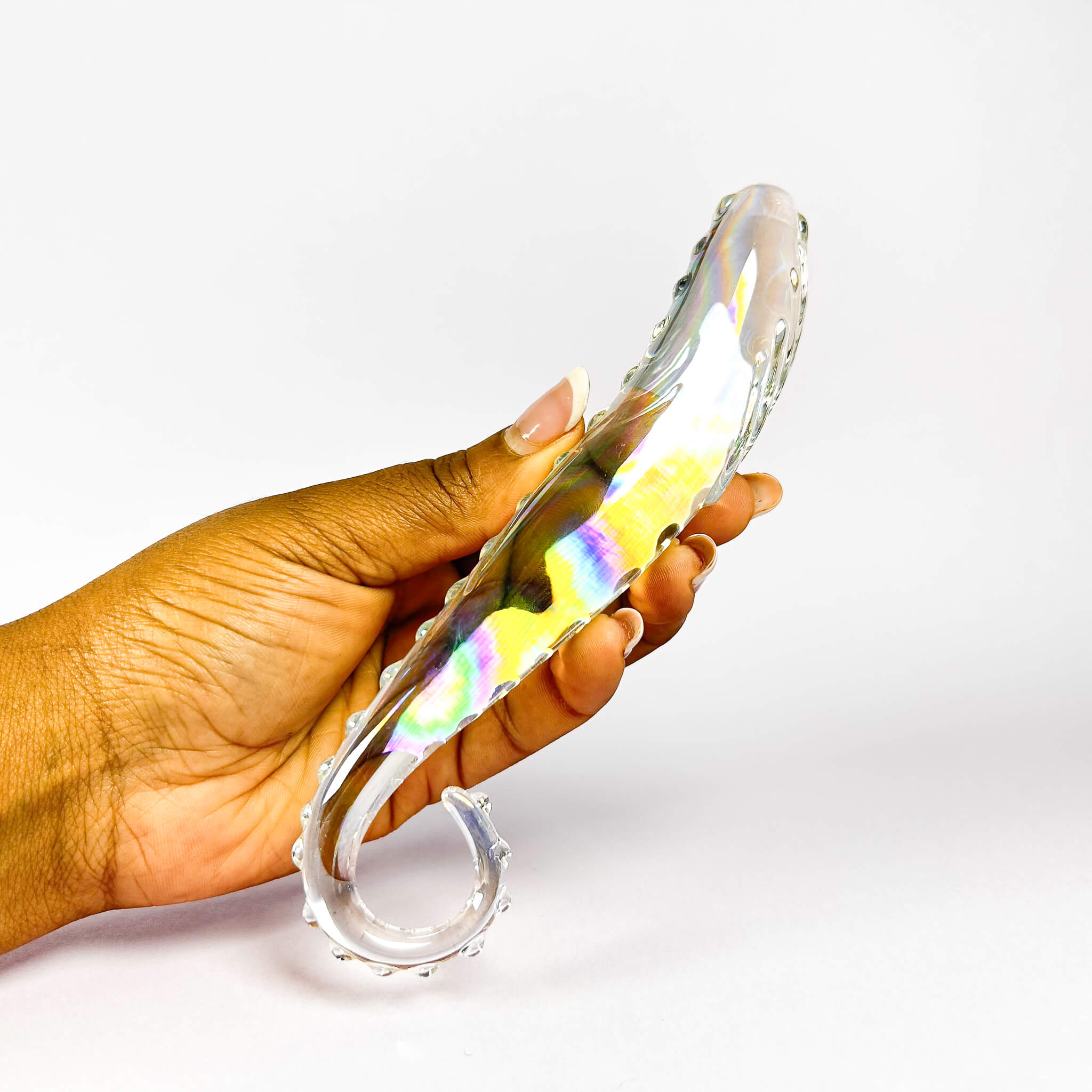 Hand holding a glass dildo with a colorful, wavy design on a white background