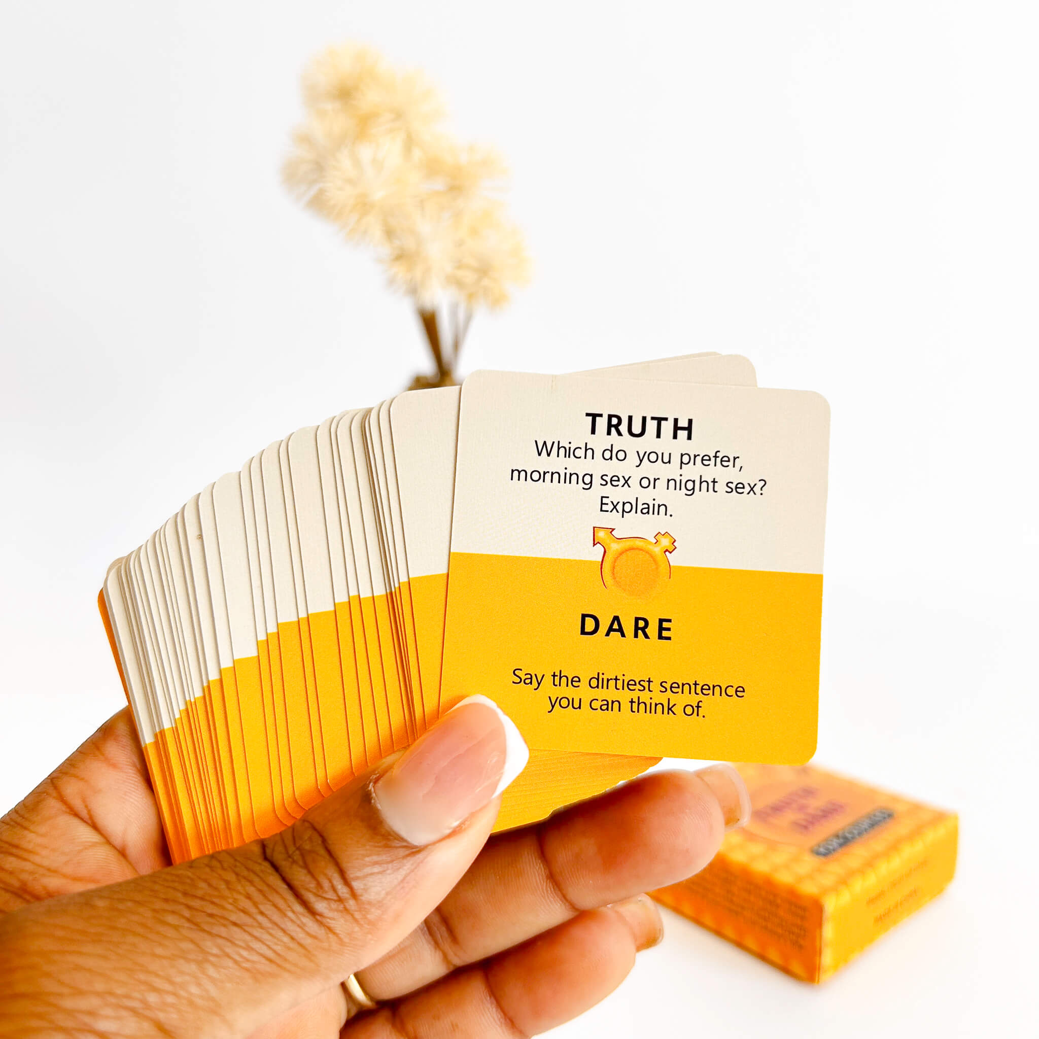 Hand holding a deck of cards with 'Truth' and 'Dare' questions on a white background