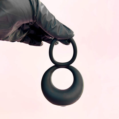 Black cock ring held by a gloved hand on a light pink background