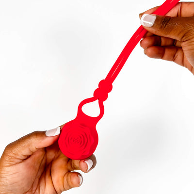 Red silicone adjustable vibrating cock ring  with a holder being held by two hands on a white background
