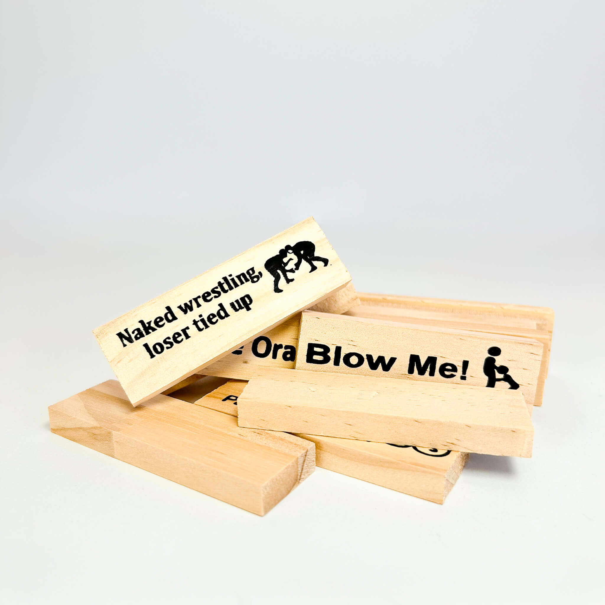 Wooden adult jenga blocks with humorous text and graphics on a light gray background