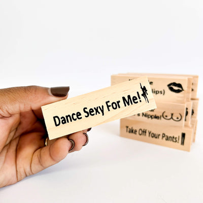 Hand holding a wooden adult jenga block with 'Dance Sexy For Me!' text, with more stamps in the background.