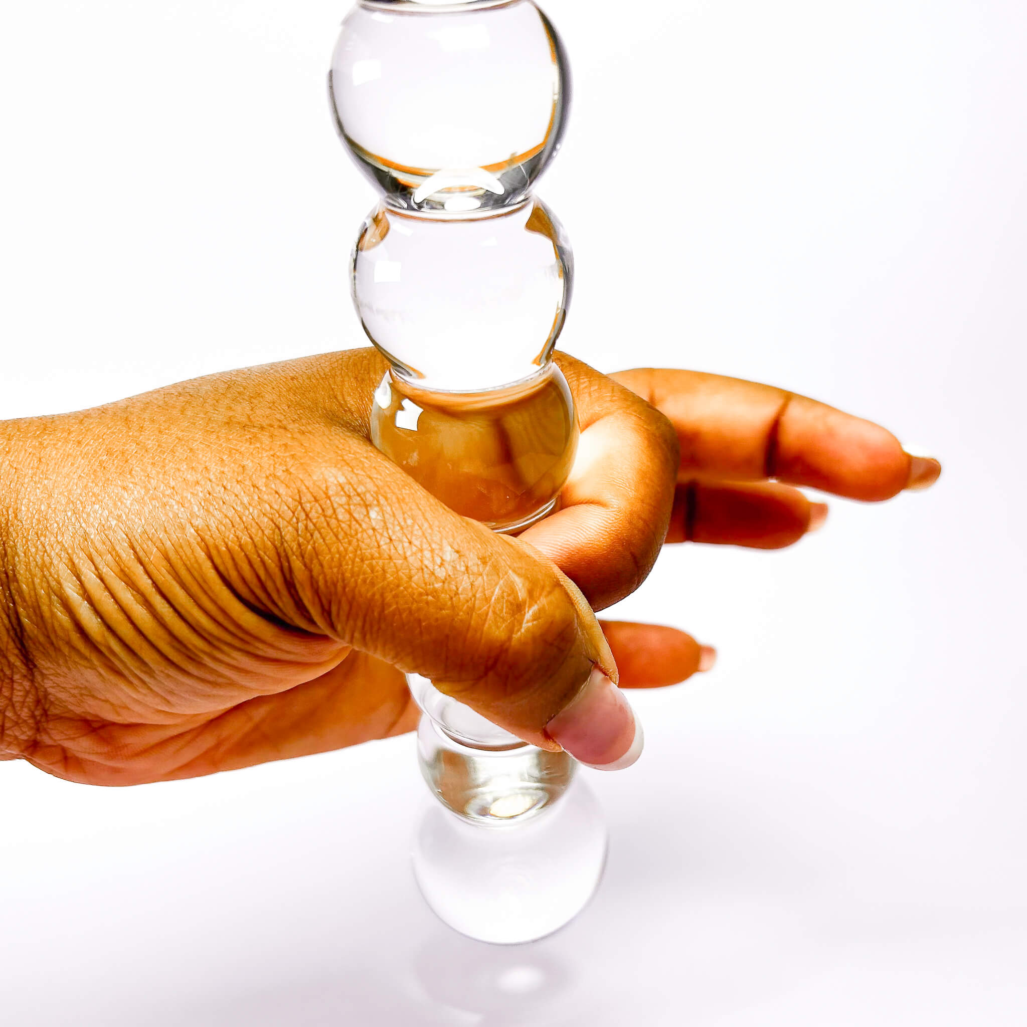 Hand holding a clear glass dildo with beads against a white background