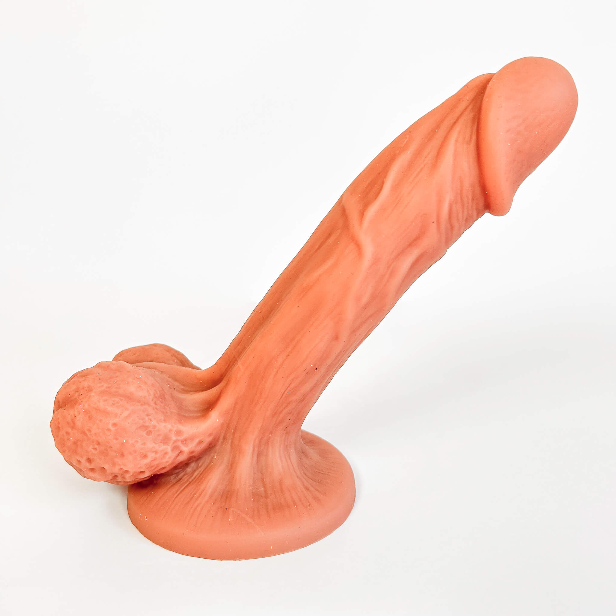 An adult novelty product depicting a realistic, flesh-toned penis with a textured, wrinkled surface and a separate realistic textured foreskin, mounted on a round base against a plain white background.