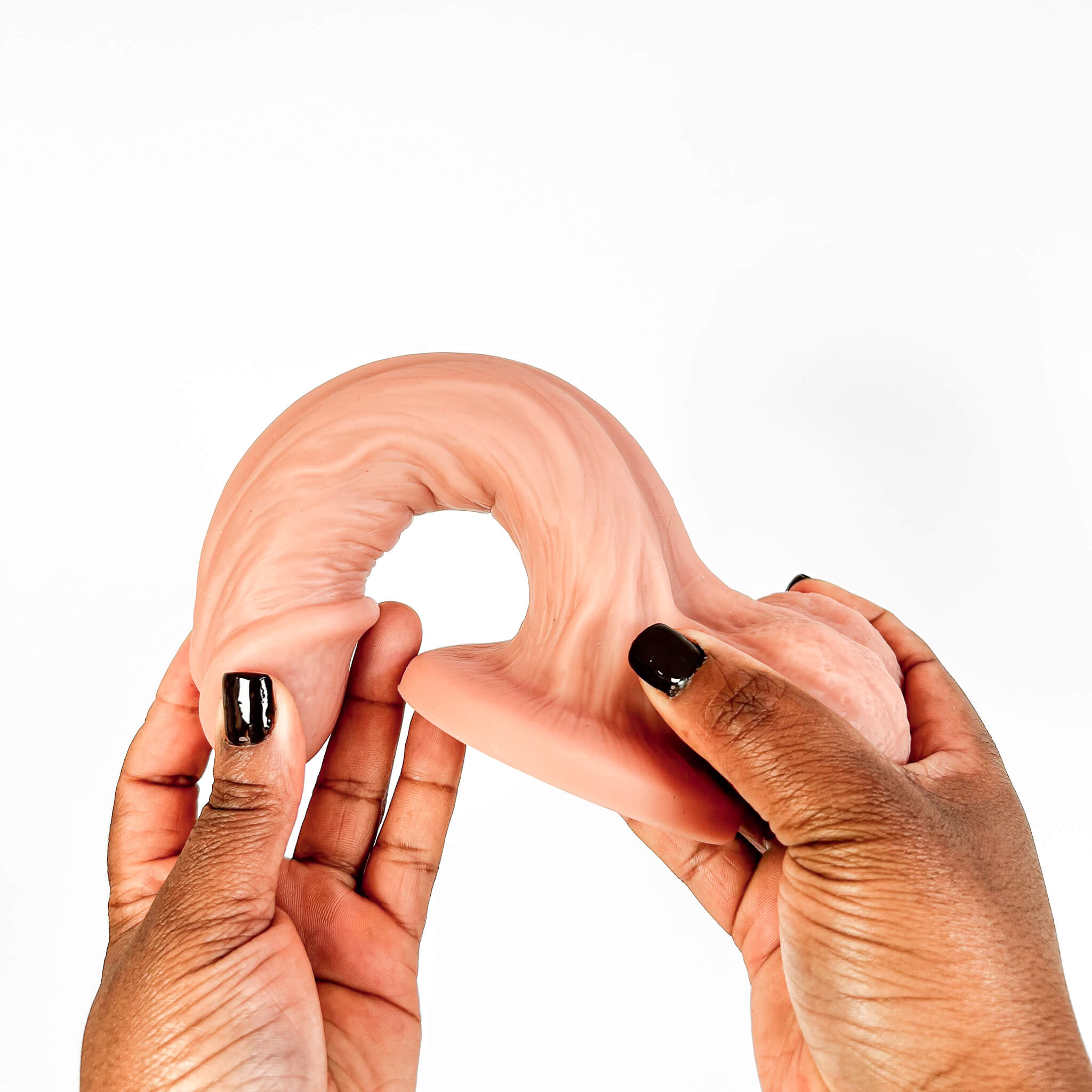 A curved, flesh-toned silicone intimate product being held between two hands against a plain white background.
