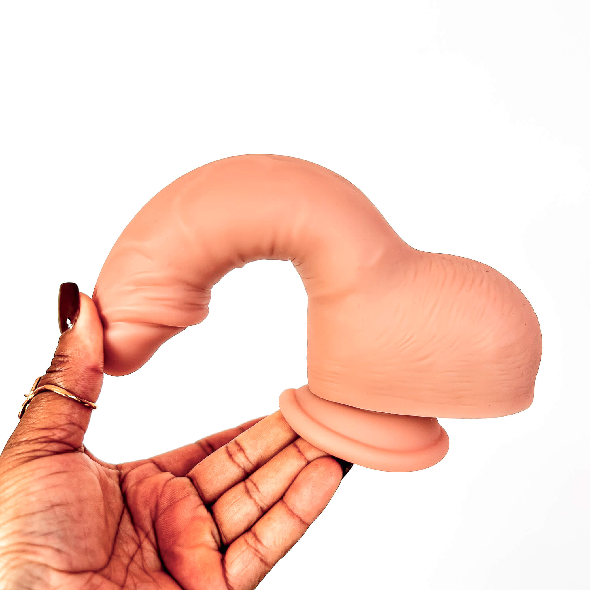 A flesh-toned silicone adult novelty item being held in a person's hand against a plain white background.