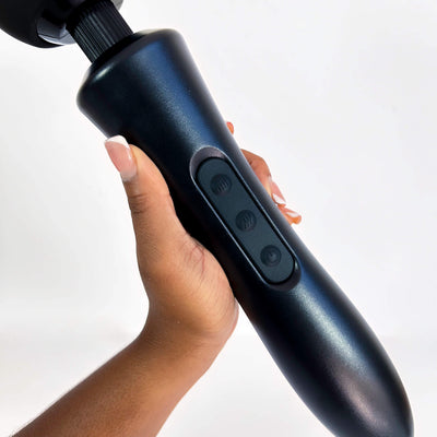 Hand holding a black wand vibrator with buttons on a white background