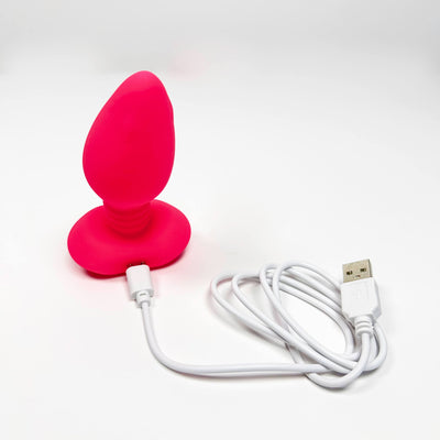 Pink silicone booty rocker butt plug vibrator with a USB cable on a white background