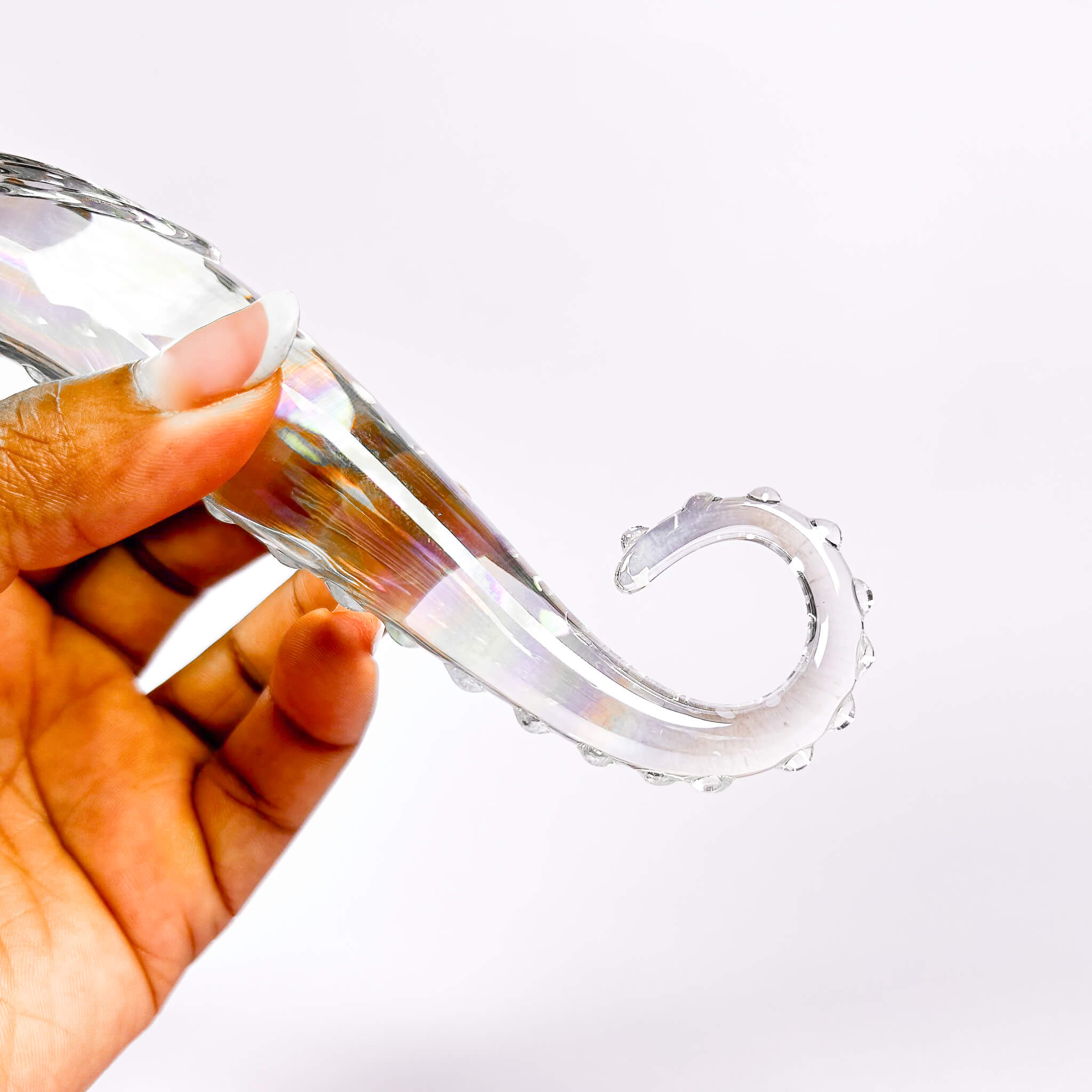 Clear glass dildo held by a hand on a white background