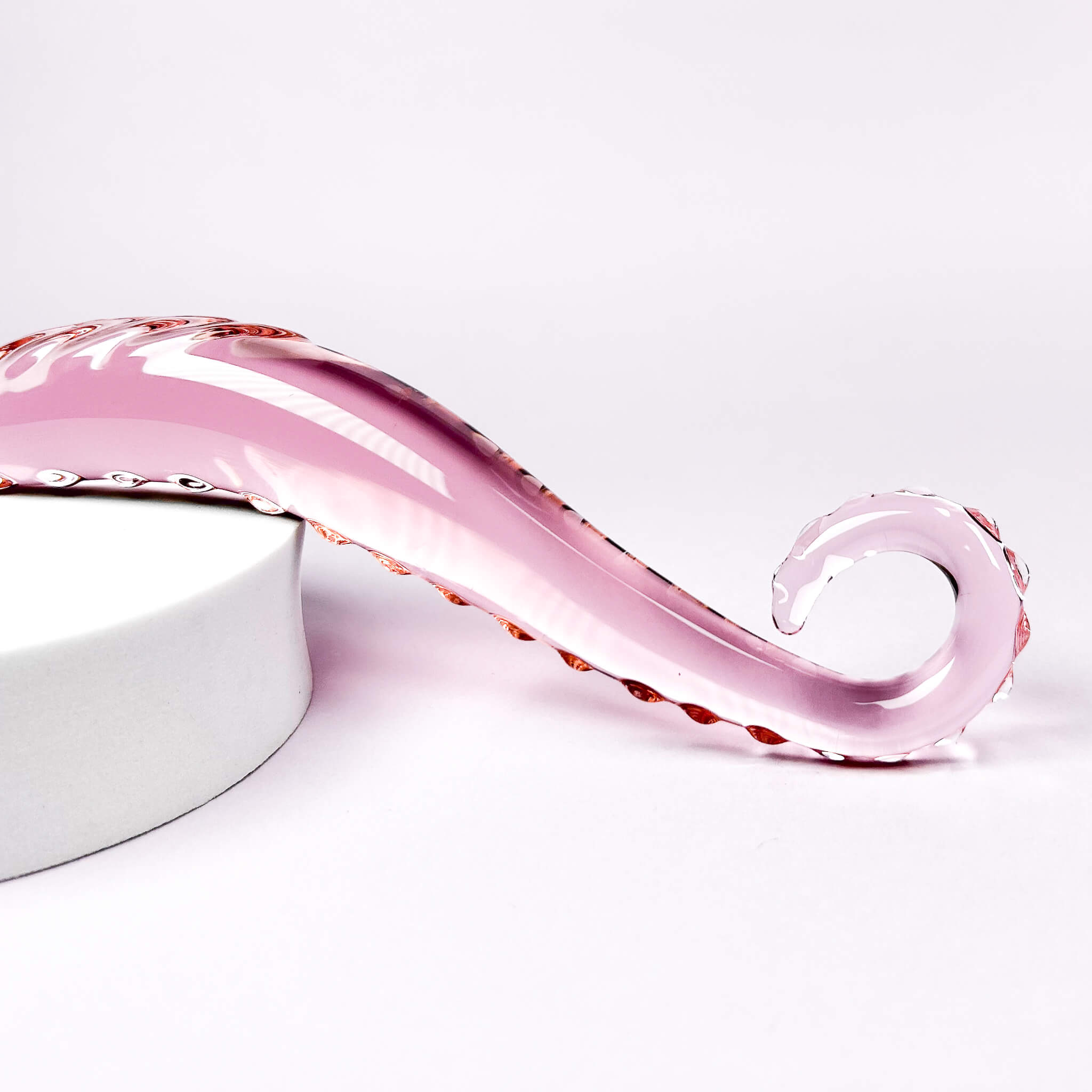 Pink glass curved dildo with wavy design on a white background