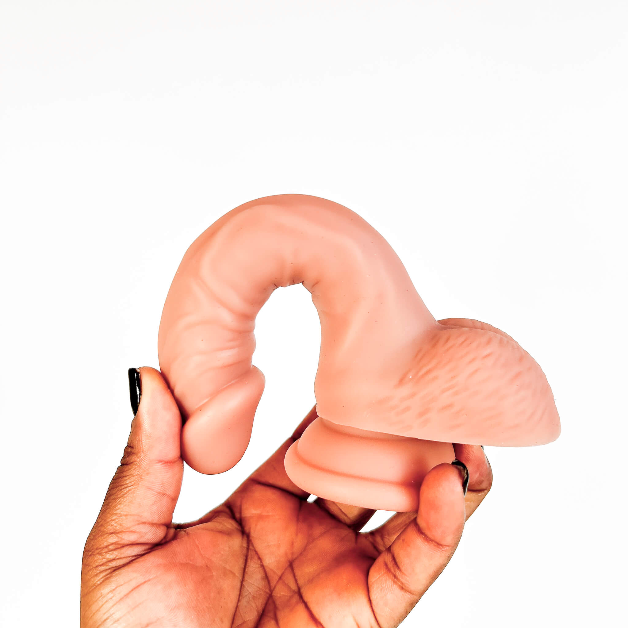 A flesh-toned silicone adult novelty item being held in a hand against a plain white background.
