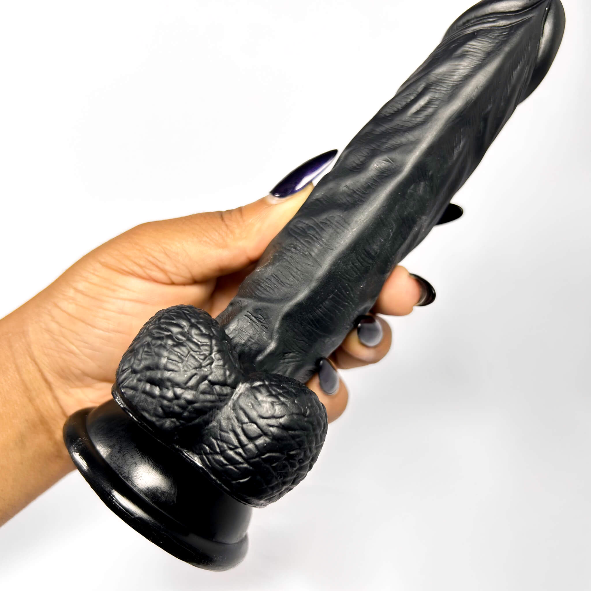 Black dildo adult toy held by a hand on a white background