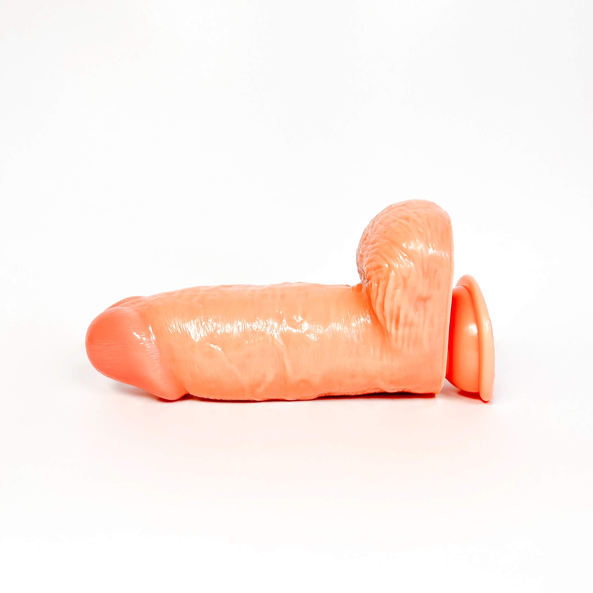 An flesh extra thick dildo with a textured shaft, flared base, and curved, hair-like rear attachment, photographed on a seamless white background.