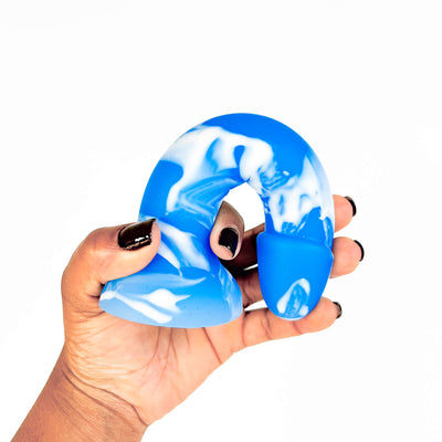 A hand with black nail polish holds a blue and white marbled silicone dildo against a plain white background.