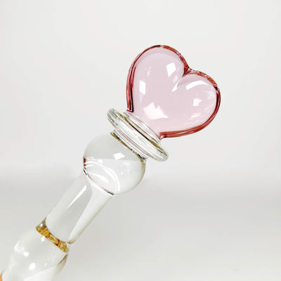 Glass dildo with a pink heart-shaped stopper on a white background
