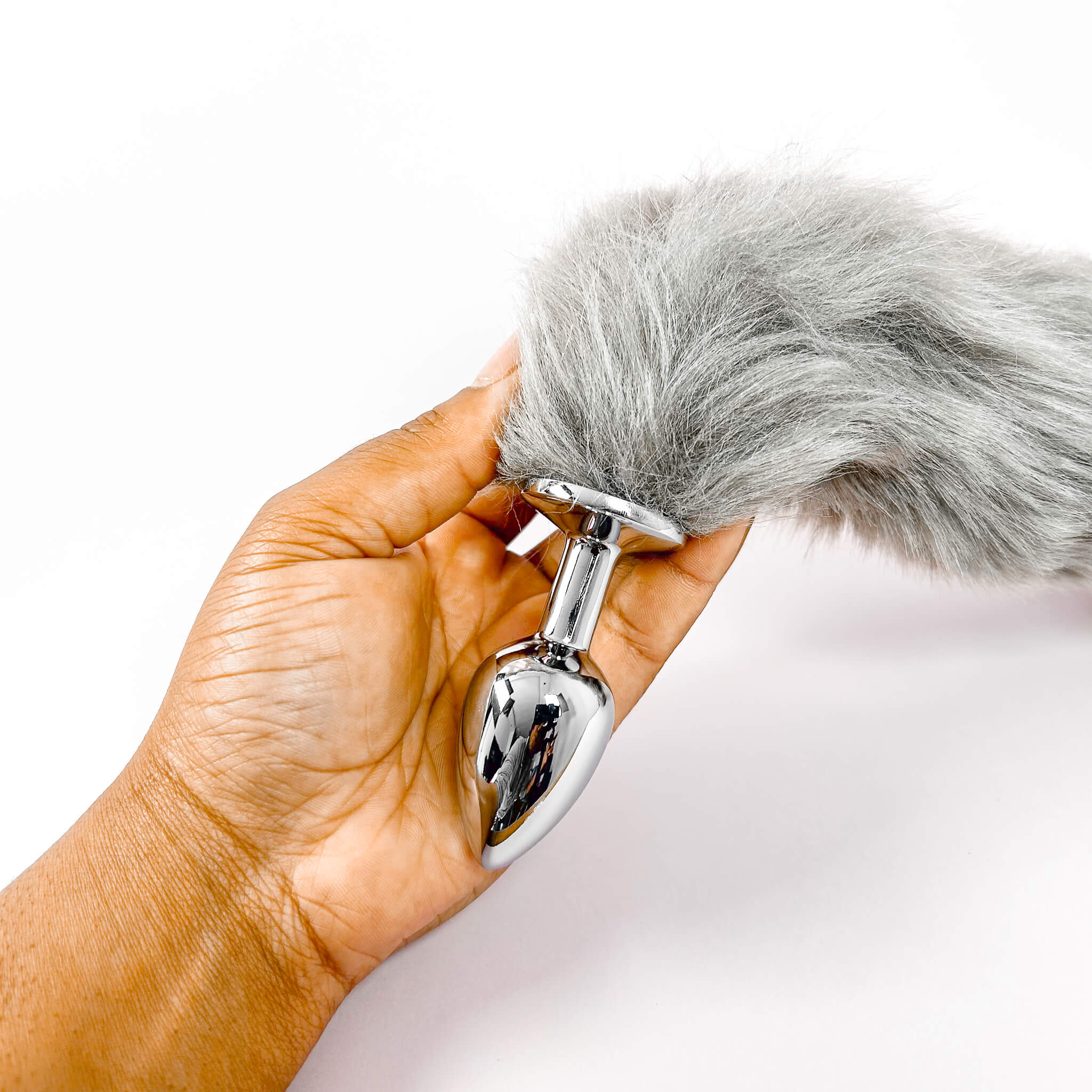 Hand holding a metal butt plug with a gray fur-like top against a white background