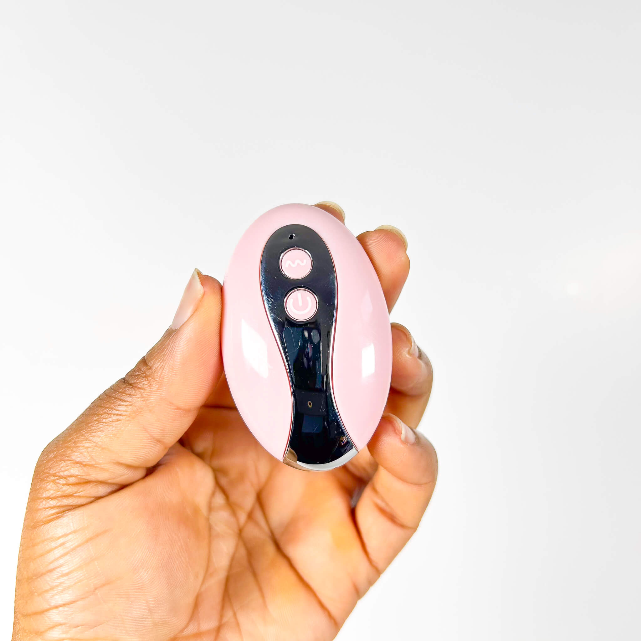 Hand holding a pink and silver vibrator remote against a white background