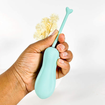 Hand holding a light blueinsertable remote vibrator with a floral head against a white background