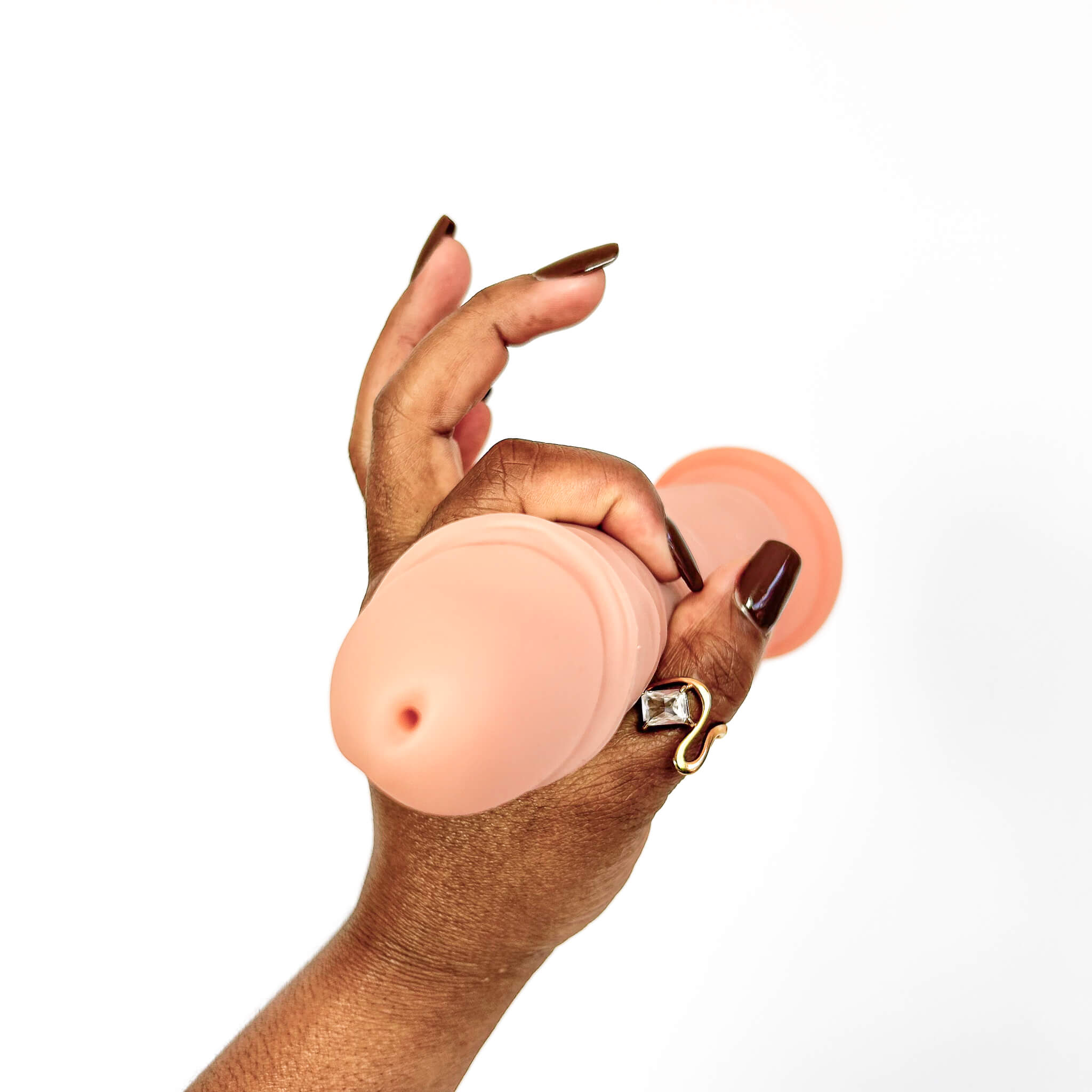 A hand with dark brown manicured nails holds a peach-colored silicone personal massager against a plain white background.
