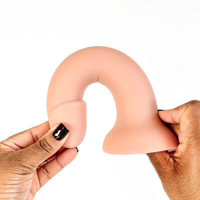 A flesh-toned silicone curved dildo being held by two hands against a plain white background.