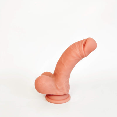 A realistic flesh-toned dildo with a curved shaft, textured surface, and suction cup base, photographed on a plain white studio background.