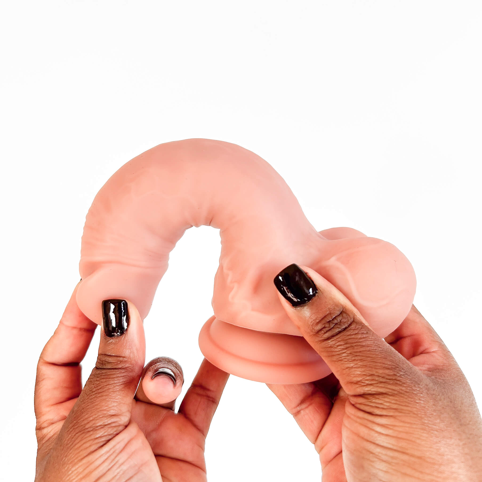 A flesh-toned silicone adult novelty product being held between two hands with black nail polish, photographed against a plain white background.