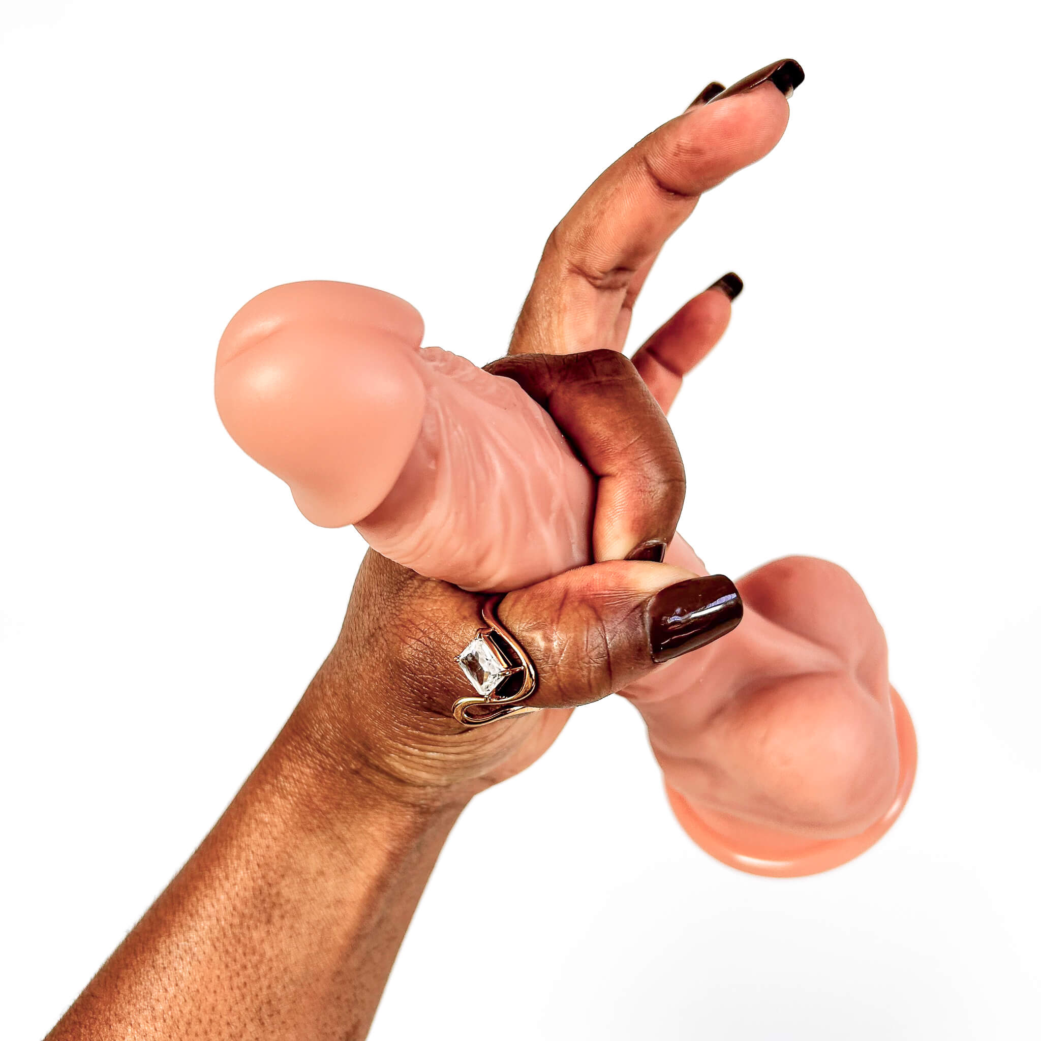 A close-up of a hand holding a realistic dildo against a plain white background.